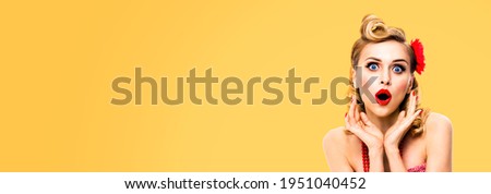 Unbelievable news! Excited surprised, very happy blondy hair woman. Pin up syle girl with opened mouth and raised hands. Retro and vintage concept. Orange yellow background. Wide composition image.