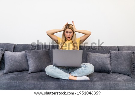Shocked attractive woman looking with amazement at laptop screen, sitting on sofa at home, cute girl with wide opened eyes watching movie or video in social network, surprised by internet news