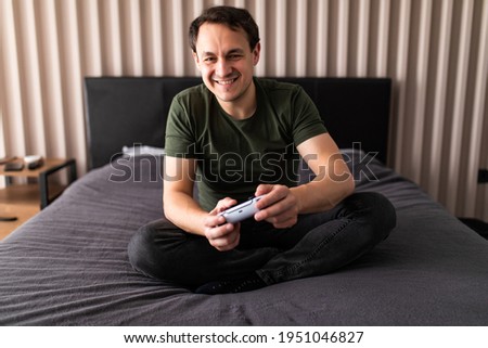 Attractive man holding joy stick and playing videogames on tv at vacation, sits at home on the cozy couch