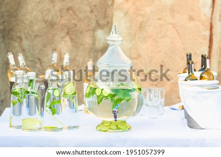 Table with fresh lemonade in beverage dispenser and bottles at outdoors cafe or catering