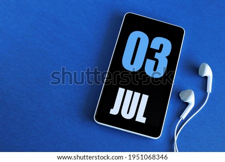 July 03. 3 st day of the month, calendar date. Smartphone and white headphones on a blue background. Place for your text. Summer month, day of the year concept.