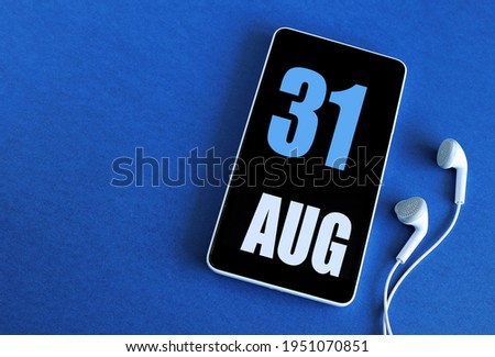 August 31. 31 st day of the month, calendar date. Smartphone and white headphones on a blue background. Place for your text. Summer month, day of the year concept.