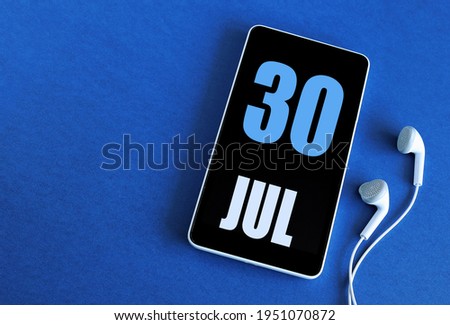 July 30. 30 st day of the month, calendar date. Smartphone and white headphones on a blue background. Place for your text. Summer month, day of the year concept.