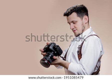photographer with camera on brown background, successful professional male looks at photos on screen of camera. photography concept.