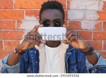 Portrait close up of stylish young african american man stretching his hands for taking selfie by smartphone on a city street