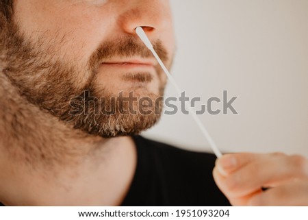 Man with beard inserts test stick for corona test into his nose to carry out a self-test for COVID-19