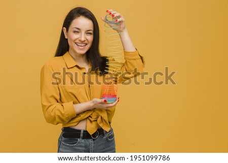 Photo of cute female holds slinky and plays with it. Wears yellow shirt, isolated yellow color background.