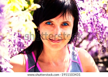 Beautiful and happy brunette girl with blue lenses on the background of blossoming Wisteria, bright contrast photography