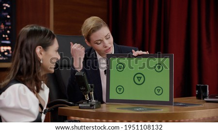 Attractive late-night talk show female host showing a green board with tracking points to celebrity guest in a studio. TV broadcast style show