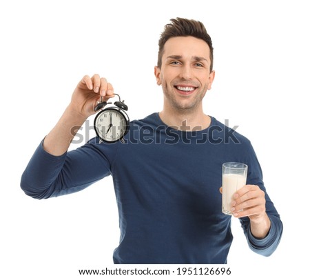Young man with glass of milk and alarm clock on white background