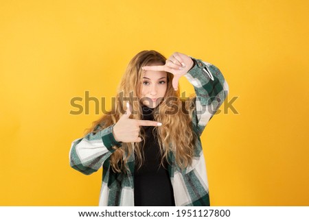 pretty blonde woman takes pictures with an imaginary camera yellow background