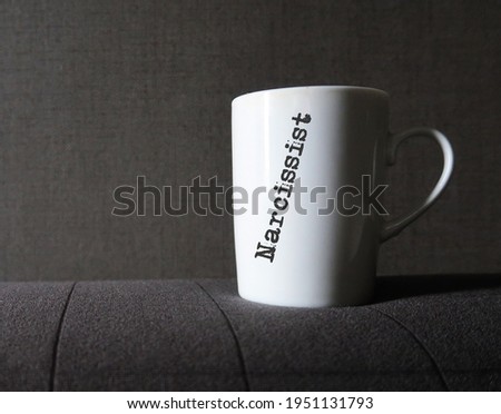 White coffee mug on dark gray background with printed text NARCISSIST, type of personality disorders, self-centered people who need attention and admiration , lack empathy to others Royalty-Free Stock Photo #1951131793