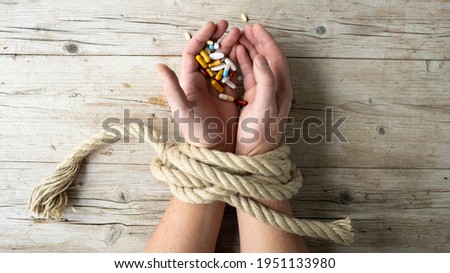 Hands of man are tied with a rope and in his hands he holds many different pills, concept addiction, drug addiction, photo taken from above Royalty-Free Stock Photo #1951133980