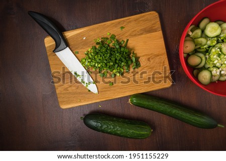 The cut spring onion is on cutting board. The dark food photography of cut green onion and cucumber.  The flat lay of vegetables on the kitchen table. 