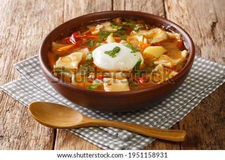 Delicious Pancutras or Pantrucas soup with vegetables, ground beef, noodles and poached egg close-up in a bowl on the table. horizontal
