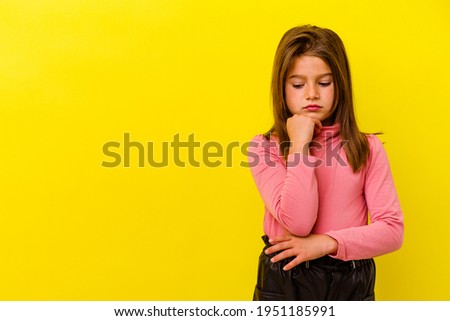 Little caucasian girl isolated on yellow background looking sideways with doubtful and skeptical expression.