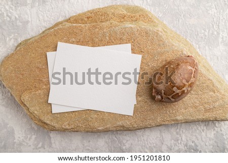 White paper business card, mockup with natural stone and seashell on gray concrete background. Blank, flat lay, top view, still life, copy space.