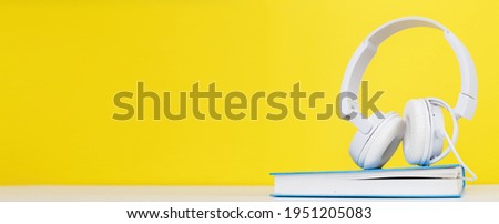 Audio book concept with modern white headphones and hardcover book on a yellow background. Listening to a book. E-learning. Copyspace. banner