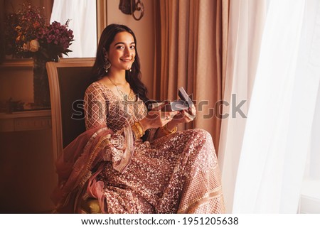 Beautiful Indian woman in a fancy traditional outfit opening the box with present in the luxury five star hotel room, looking at camera Royalty-Free Stock Photo #1951205638