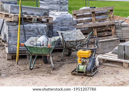Road and pavement constuction work site with bricks piles, rammer machine and carts. Stock photo