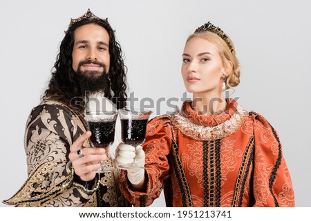 interracial historical couple in crowns holding glasses of red wine isolated on white