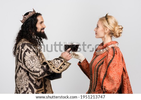 interracial historical couple in medieval clothing and crowns clinking glasses of red wine isolated on white