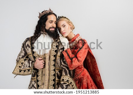 blonde queen in crown hugging hispanic king in medieval clothing isolated on white