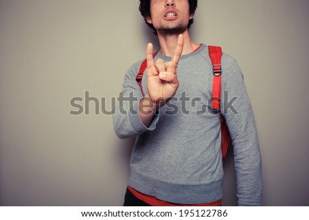 Young man wearing a red backpack is displaying a heavy metal gesture