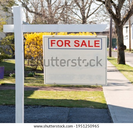 A wood post holding a sign that reads for sale with the rest blank on the front lawn of a residential home.
