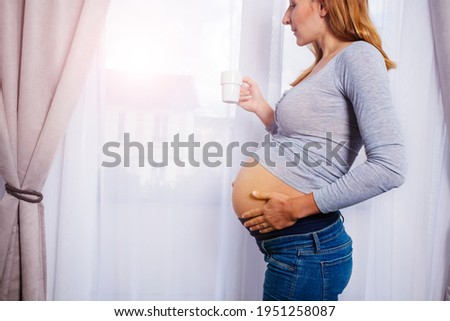 Pregnant woman drink coffee stand by the window