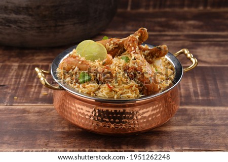 Dum chicken biriyani, close up image of Kerala-Thalassery biriyani  which is mixed with masala and yellow in colour arranged in a copper serving bowl   placed on wooden textured background. Royalty-Free Stock Photo #1951262248