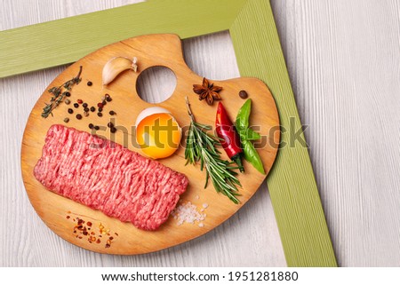 Mince - ground meat, egg, pepper, basil, rosemary, spices on palette artist above picture frame. Culinary art  concept