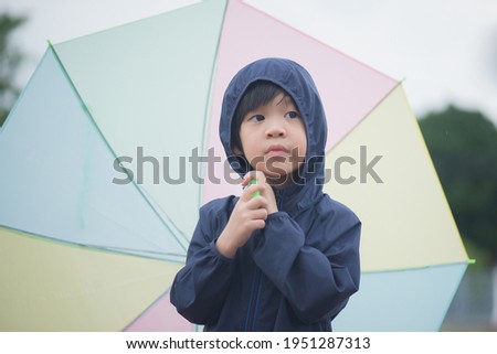 Happy asian boy holding colorful umbrella playing in the park after the rain