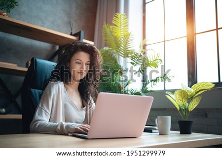 cheerful female manager working with laptop and typing at home office Royalty-Free Stock Photo #1951299979
