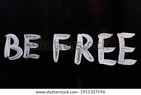 Text message 'Be free' on glass using brush and paint. Handwritten appeal motivation message 'Be free'. Black background. High quality photo