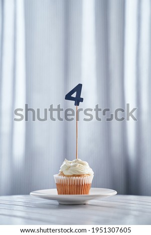 Birthday or anniversary minimalistic greeting card concept. Tasty homemade vanilla cupcake or muffin with creamy topping and number 4 four on white plate and bright background. High quality image