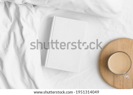 White book mockup with a cup of coffee on the bed. Royalty-Free Stock Photo #1951314049