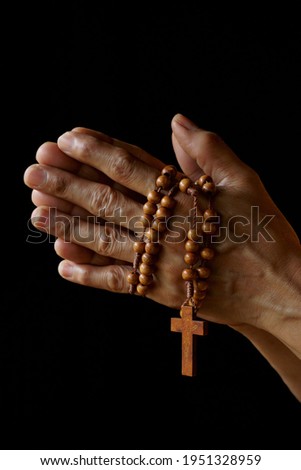 Praying hand of an old Indian Catholic woman with wooden rosary isolated on a plain black background. Royalty-Free Stock Photo #1951328959