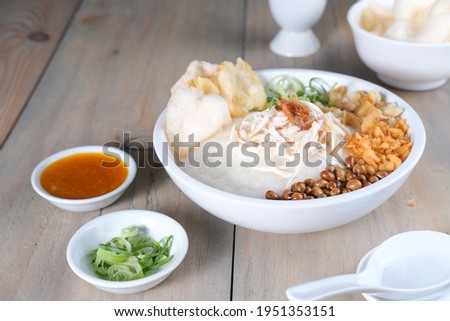 Bubur ayam or chicken congee is Chinese Indonesian rice porridge topped with shredded chicken and various savoury condiments served on white bowl and wooden table. Royalty-Free Stock Photo #1951353151
