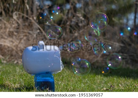 Portable soap bubble machine blowing colorful bubbles. Sunny day, selective focus.