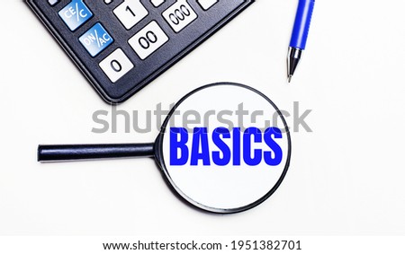 On a light background, a black calculator, a blue pen and a magnifying glass with text inside the BASICS. View from above