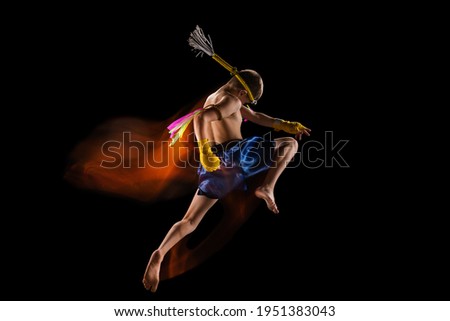 Little boy exercising thai boxing on black background. Mixed light. Fighter practicing in martial arts in action, motion. Evolution of movement, catching moment. Youth, sport, asian culture concept. Royalty-Free Stock Photo #1951383043