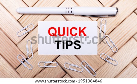 On a background of wooden blocks, a white pen, white paper clips and a white card with the text QUICK TIPS. View from above