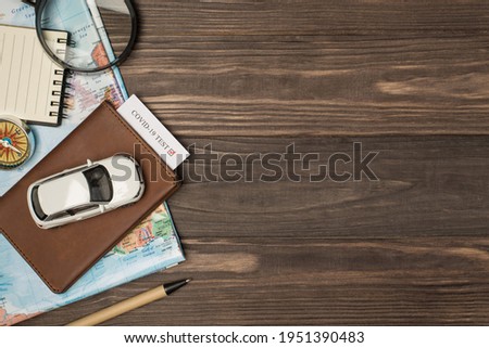 Overhead photo of brown passport with covid-19 test inside car map magnifier compass notepad and pen isolated on the wooden backdrop with blank space