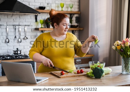 Plus size , fat caucasian woman learning to make salad and healthy food from social media adding vegetables to salad bowl ,Social distancing, stay at home concept