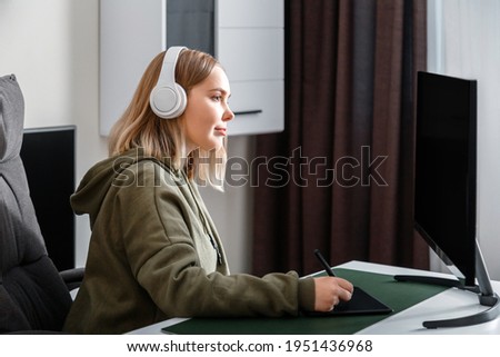 Young woman graphic designer freelancer busy working remote from home using pc computer and graphics tablet in living room interior. Casual teenager girl in draws studying animation and visual arts