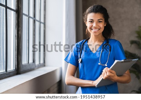 African-american doctor working in hospital , healthcare and medical concept .Stethoscope around her neck. Female black doctor filling up medical form at clipboard while standing straight in hospital
