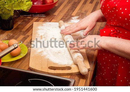 Roll out the dough. Hands with a rolling pin roll out the dough. The cooking process in the kitchen. A woman in a red dress cooks in the kitchen. Flour, eggs.