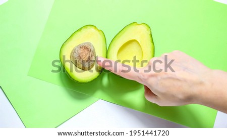 The index finger that points to the half of the avocado. The concept of dietary healthy nutrition. Top view.