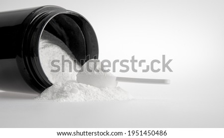 Sports nutrition -  protein. Measuring spoon and white medicinal powder with black jar on white background. Nutritional supplement or medicament, medicine treatment concept Royalty-Free Stock Photo #1951450486